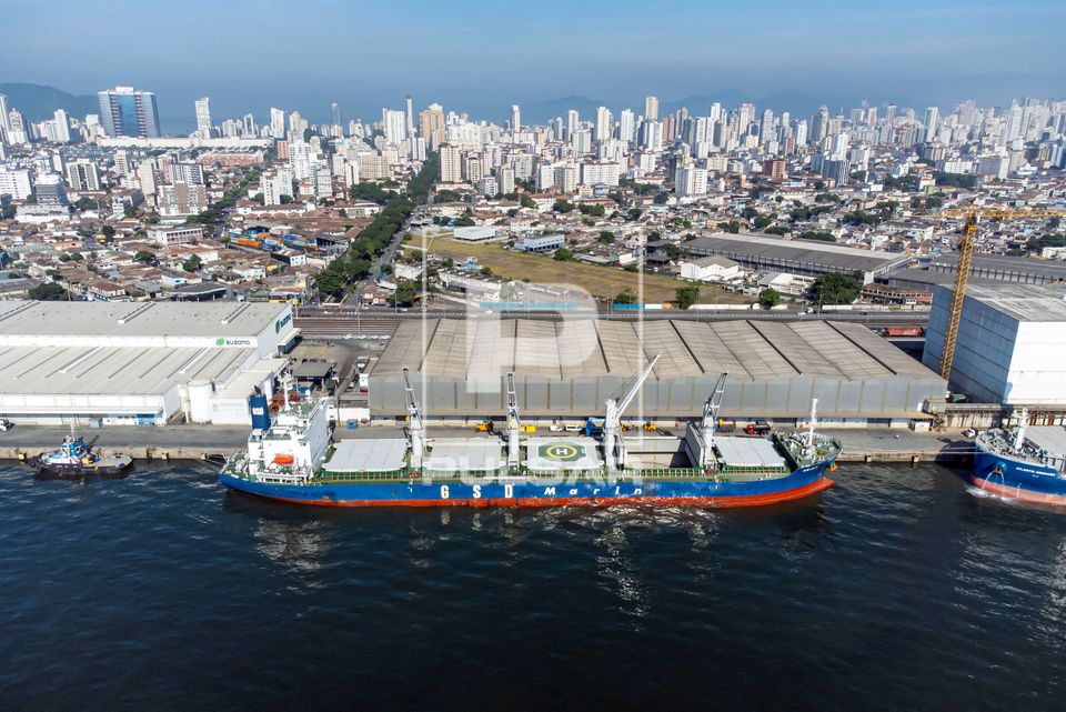 Vista de drone de navio graneleiro sendo abastecido em terminal no porto com a cidade de Santos ao fundo