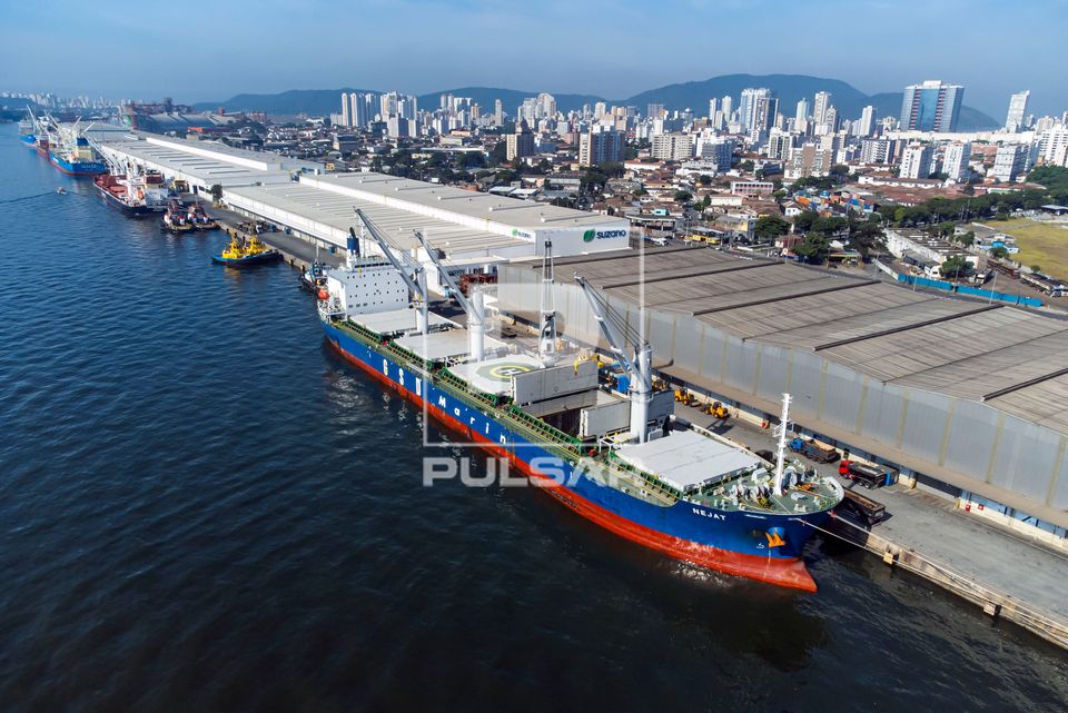 Vista de drone de navio graneleiro sendo abastecido em terminal no porto com a cidade de Santos ao fundo