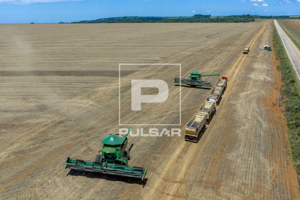 Vista de drone de colheita mecanizada de soja - ao fundo colheitadeira descarregando em caminhão graneleiro