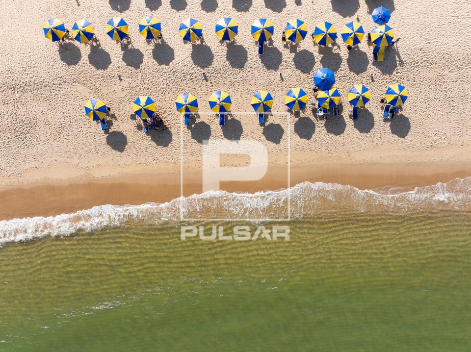 Vista perpendicular de drone de guarda-sois com turistas na Praia do Gunga