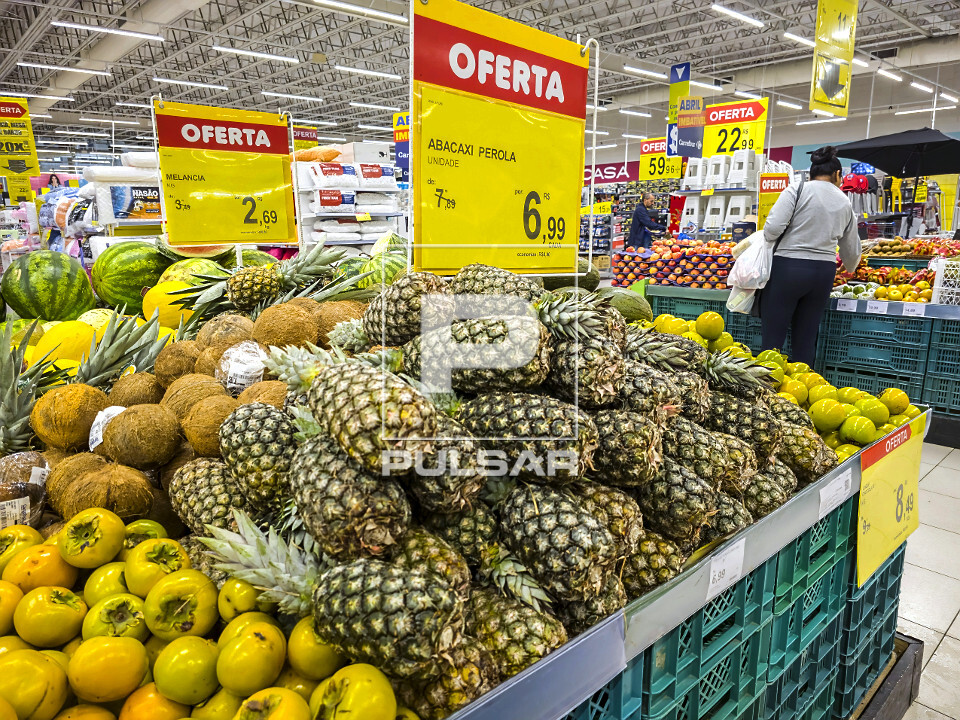 Placas de ofertas para abacaxi e melancia no setor de hortifruti de supermercado