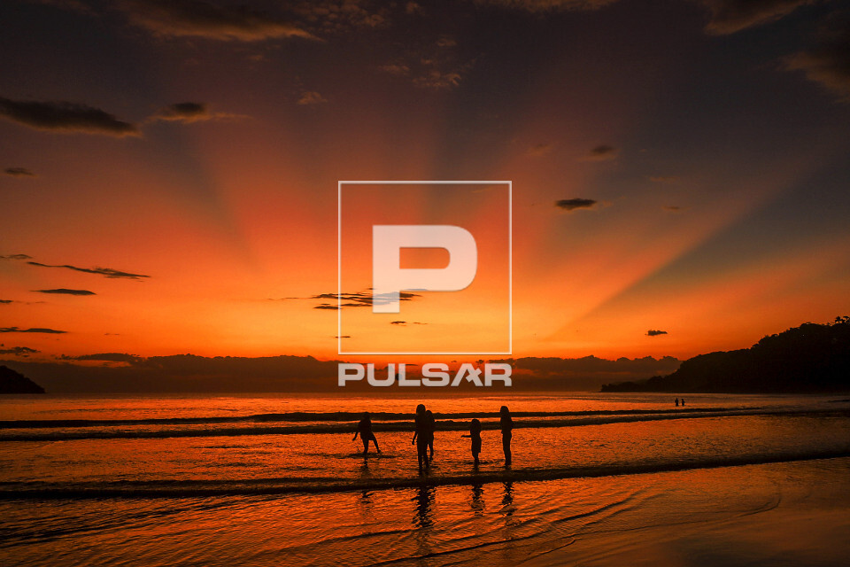 Silhueta de pessoas na Praia Barra do Sahy sob raios solares ao entardecer