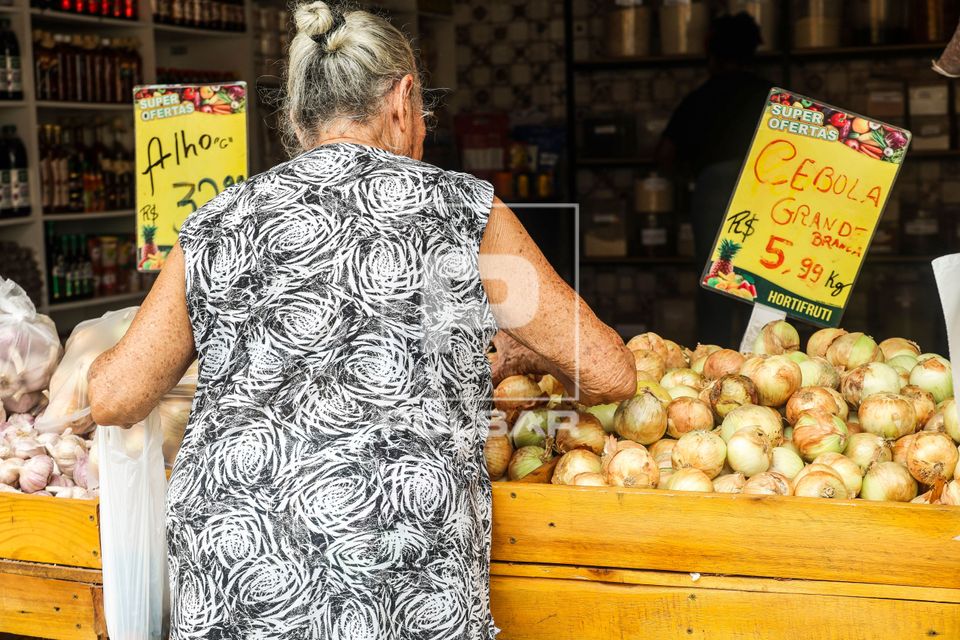 Consumidora escolhe cebolas em banca do mercado municipal