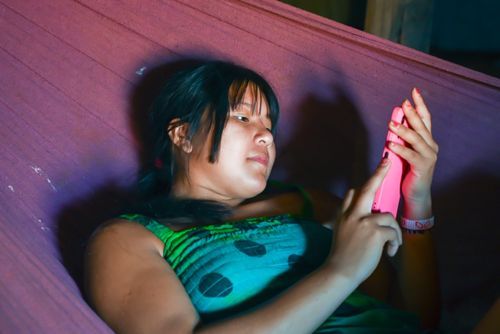 Indígena Wauja da aldeia Piyulaga deitada em rede com celular - Parque Indígena do Xingu