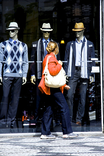 Mulher passando na frente de vitrine de loja com roupas masculinas de inverno