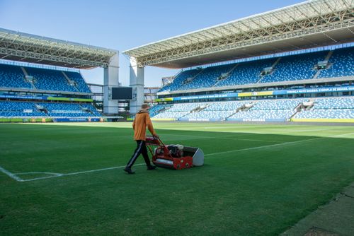 Homem aparando o gramado do campo da Arena Pantanal - estádio multiuso