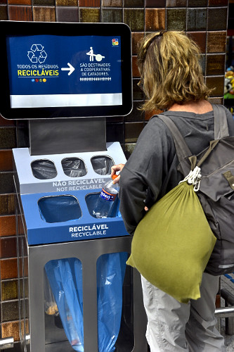 Passageira descartando garrafa de plástico em lixeira para recicláveis do Aeroporto Internacional do Recife/