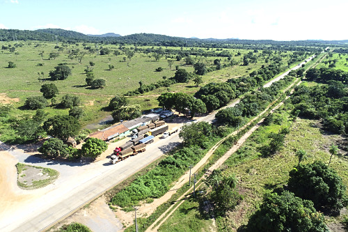 Vista de drone de trevo e caminhões estacionados na margem da Rodovia BR-364 com área de pastagem ao fundo -